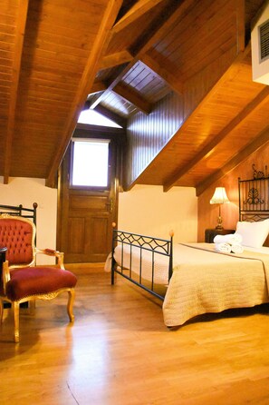 Une pièce avec un plafond en bois, un lit recouvert d’une courtepointe blanche, un fauteuil rouge rembourré et une table de chevet avec une lampe.