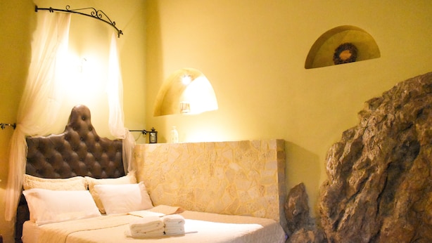 A bed with a headboard, a stone wall, and a wall-mounted lamp.