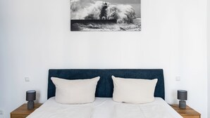 Een slaapkamer met een bed, twee nachtkastjes en een aan de muur bevestigd schilderij van een vuurtoren.