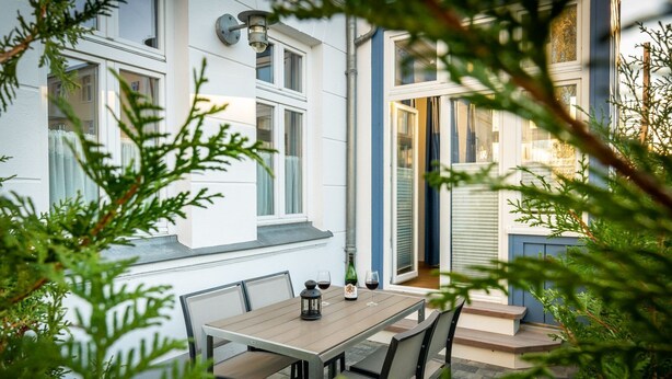 Een terras met een tafel en stoelen, een fles wijn en een lantaarn.