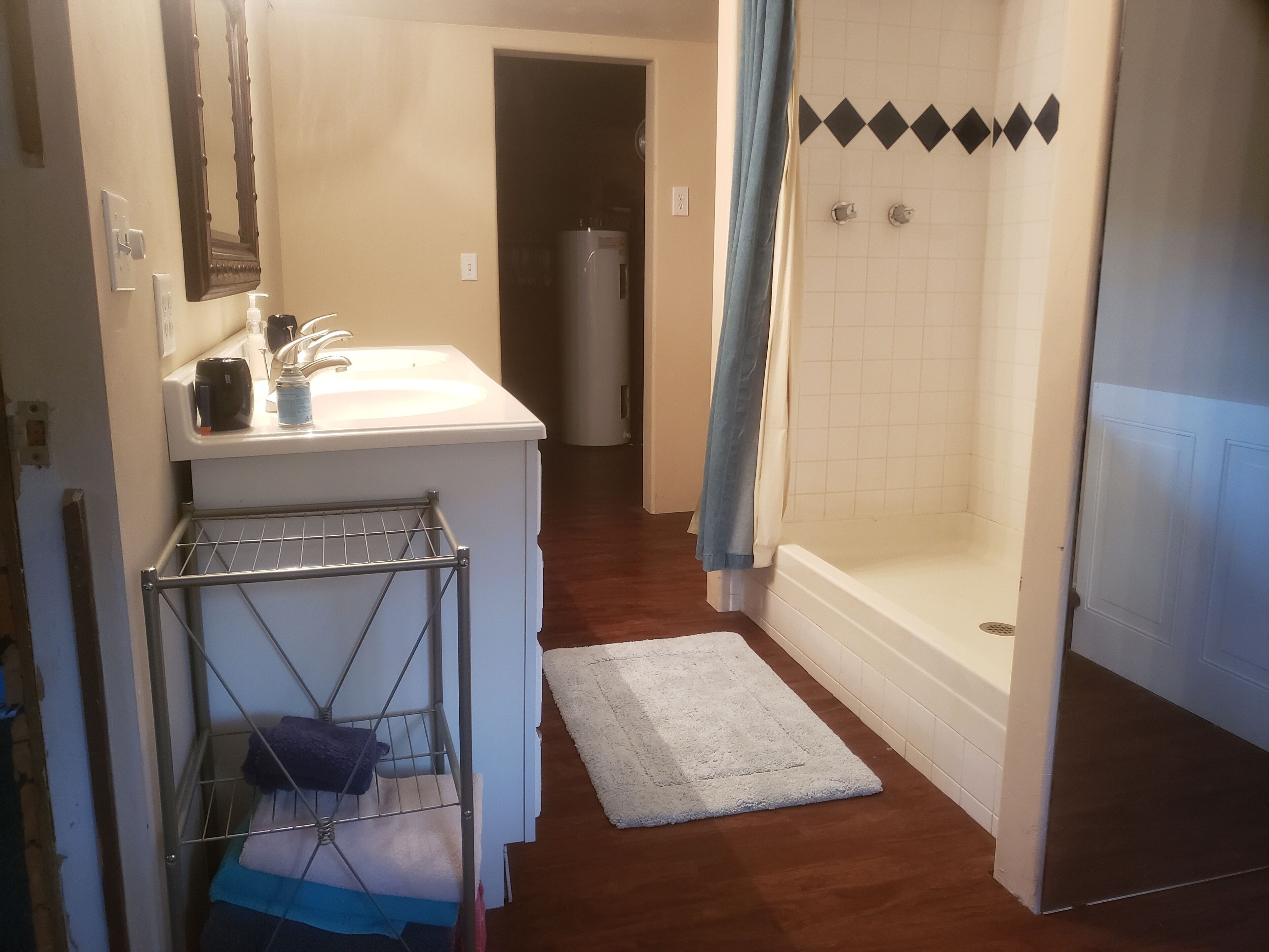 A bathroom with a sink, mirror, towel rack, shower, and a white bathtub.