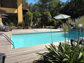 A swimming pool with a wooden deck, lounge chairs, and umbrellas.