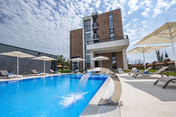 A modern building with a swimming pool, sun loungers, and umbrellas.