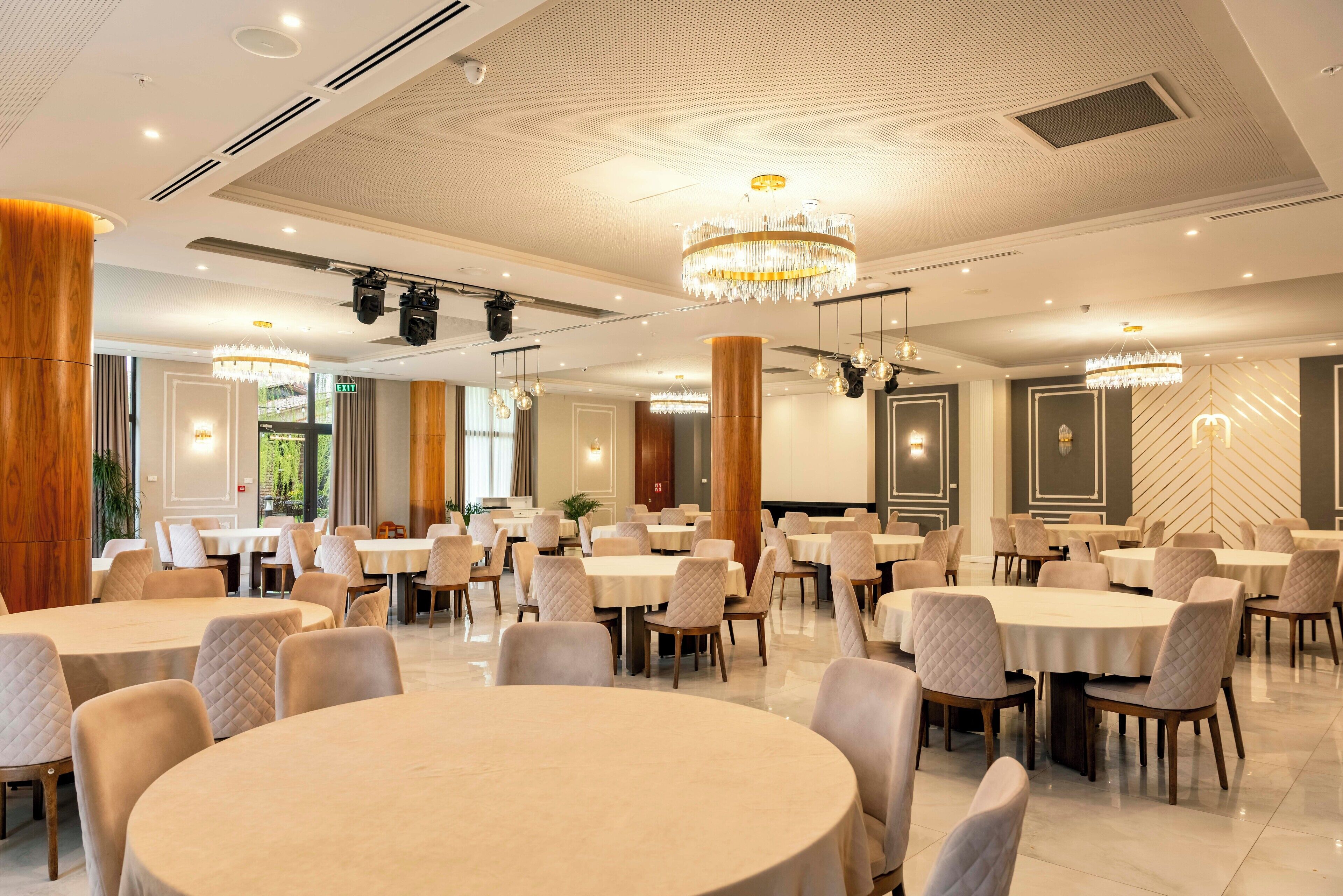 Un vaste espace dédié à la salle à manger, avec des tables et des chaises rondes, des lustres et un design de plafond moderne.