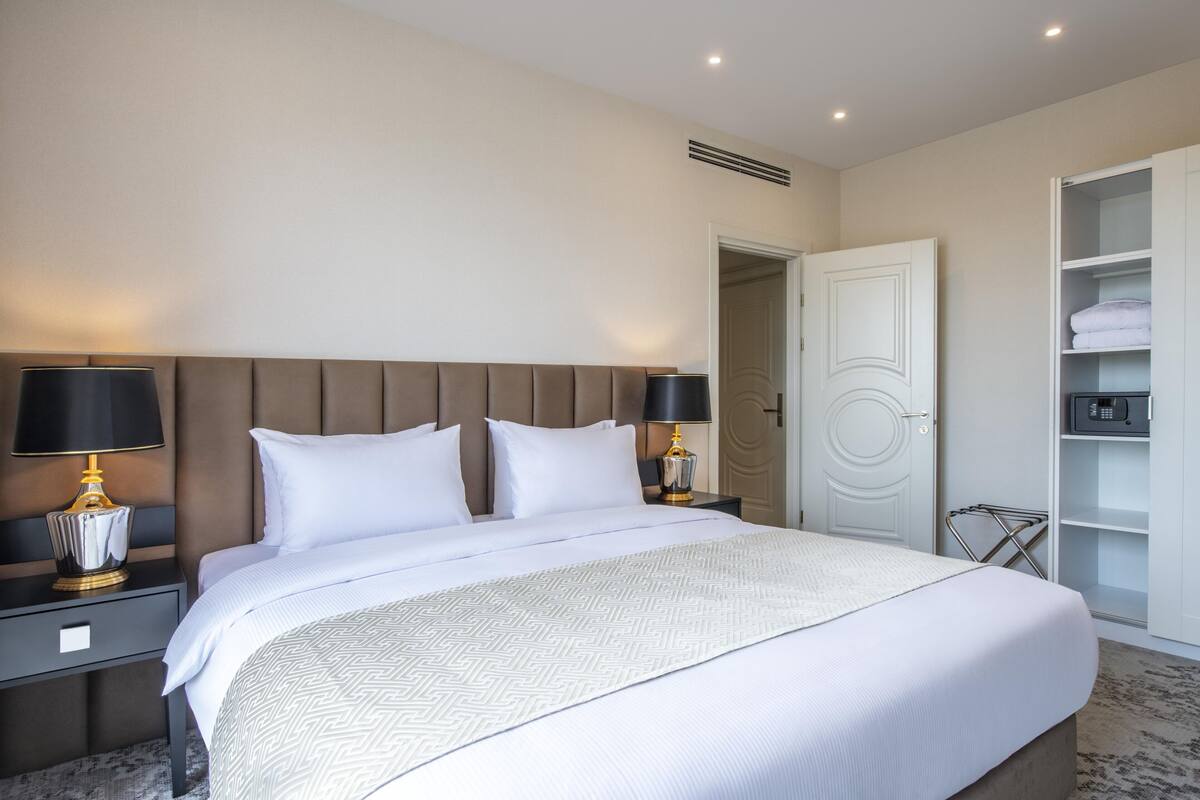 A neatly made bed with a patterned bedspread, two bedside lamps, and a white wardrobe with shelves.