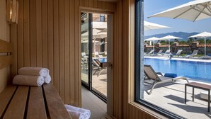 A wooden interior with a bench and towels, a glass door leading to an outdoor pool area with lounge chairs and umbrellas. - Villa Mosavali (Mtskheta)