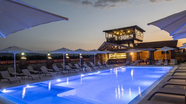 A swimming pool with lounge chairs and umbrellas, a wooden structure with a balcony, and a stone wall in the background. - Villa Mosavali (Mtskheta)
