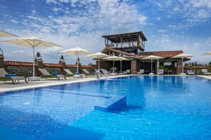 A swimming pool with lounge chairs and umbrellas, a wooden deck, and a stone building in the background.