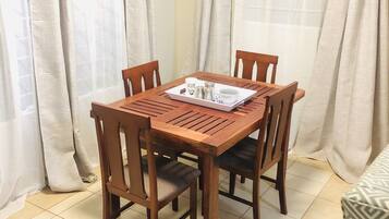 A dining area with a wooden table and chairs, a tray with condiments, and light-colored curtains.