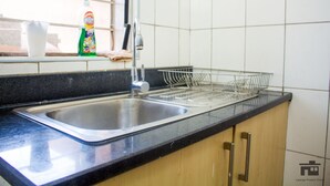 Ett kök med en diskho i rostfritt stål, ett diskställ och ett fönster. På bänkskivan står en flaska diskmedel.