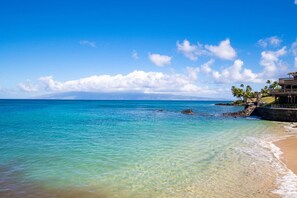 A beach with clear turquoise water, a rocky shoreline, and a building with a balcony overlooking the ocean. - Kahana Sunset E2:  Summer and Fall Savings!  Free Activities! (Lahaina)