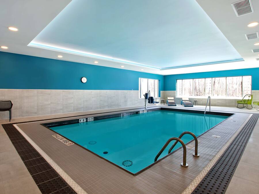 A modern indoor swimming pool with clear water, a tiled floor, and a blue wall.
