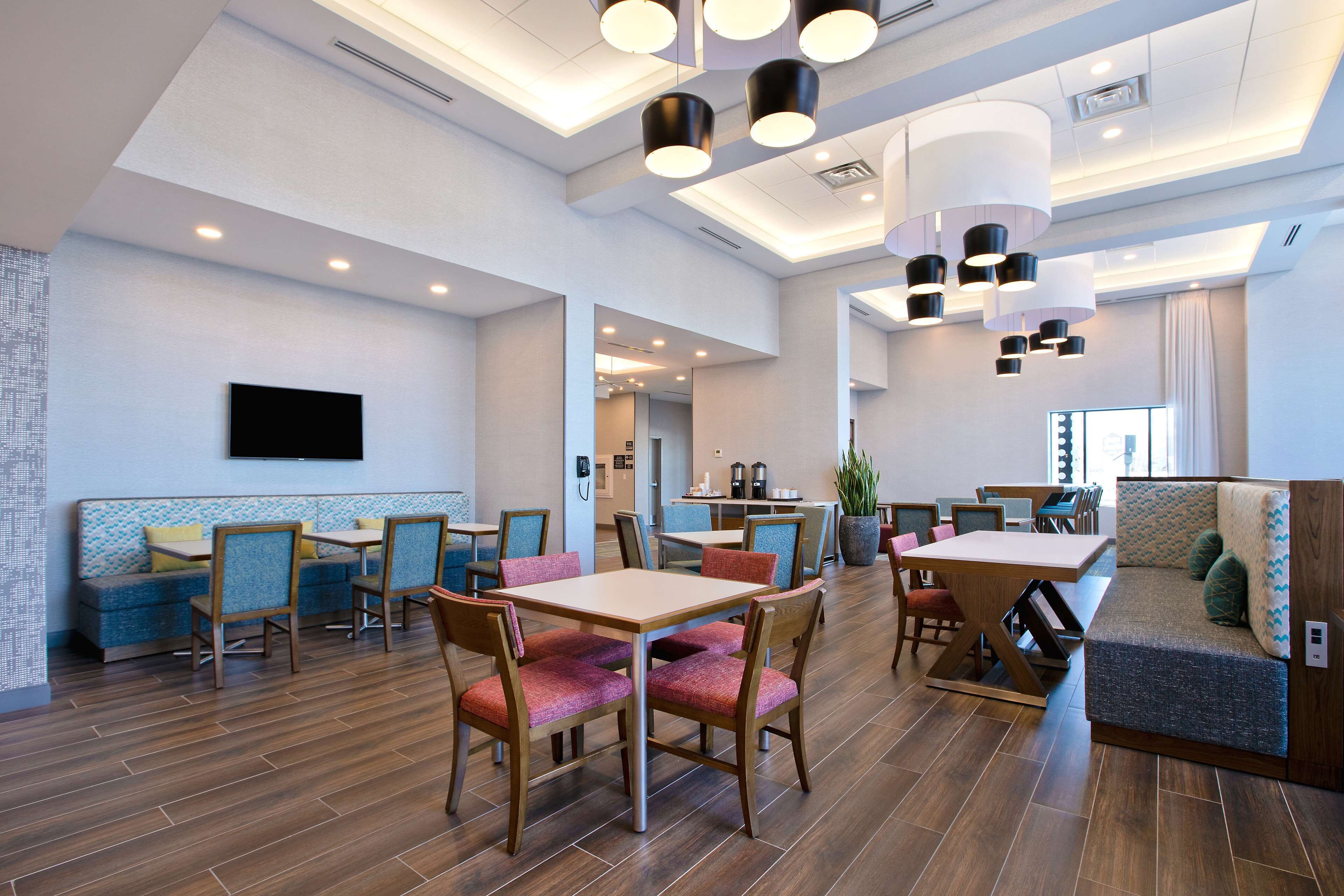 A spacious dining area with wooden tables and chairs, a seating area with cushioned benches, and a flat-screen TV mounted on the wall.