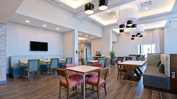 A spacious dining area with wooden tables and chairs, a seating area with cushioned benches, and a flat-screen TV mounted on the wall.