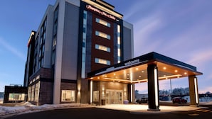 Een modern hotel met een opvallend 'Hampton Inn & Suites' bord, een overdekte ingang en een 'Welkom'-bord.