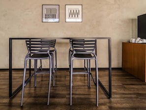 Ein minimalistisch eingerichteter Raum mit Holzboden, zwei stahlrahmenartigen Stühlen, einem Tisch und zwei gerahmten abstrakten Kunstwerken an der Wand.