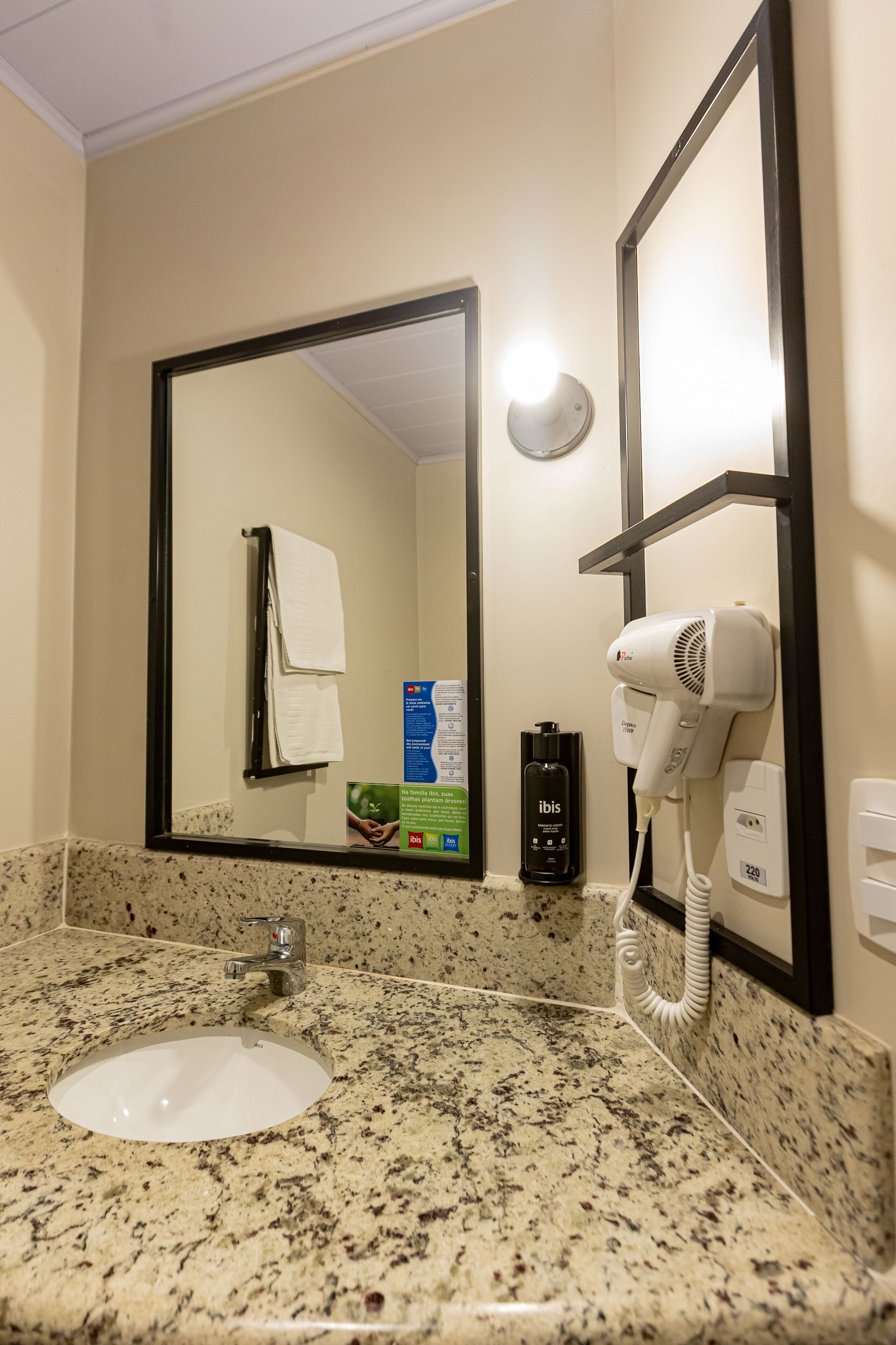 A bathroom with a granite countertop sink, a white towel hanging on a rack, a hairdryer, and a mirror with a black frame.
