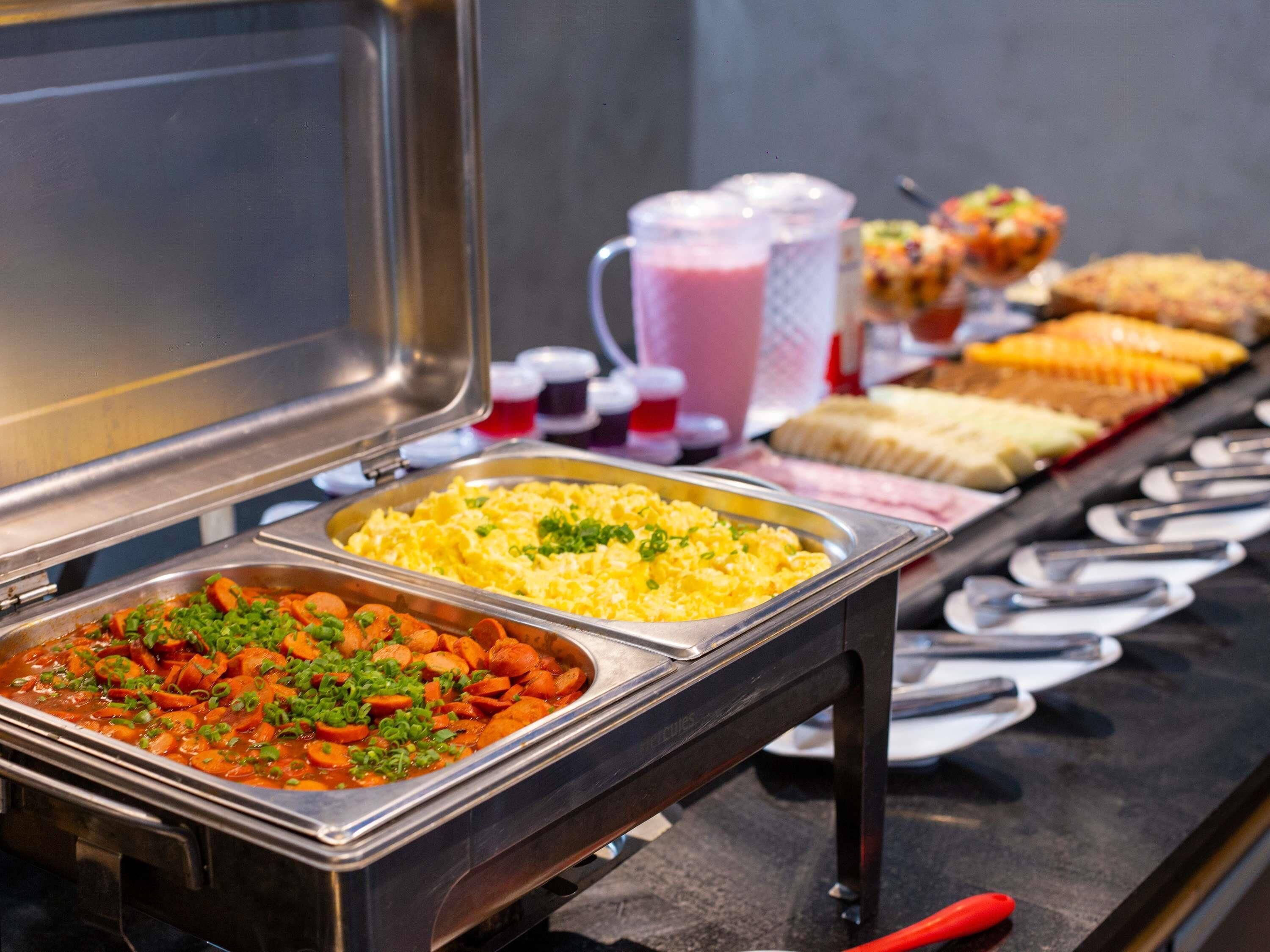 Un bufé con diversas opciones de comida, incluyendo huevos revueltos, un plato de verduras y otros alimentos preparados.