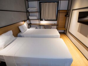 A compact hotel room with two single beds, a desk, a chair, and a TV mounted on the wall.