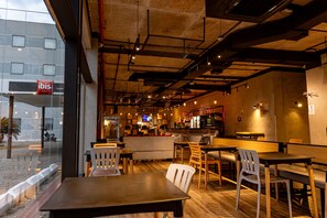 Un restaurante moderno con mesas y sillas de madera, una zona de bar y vistas a la calle.