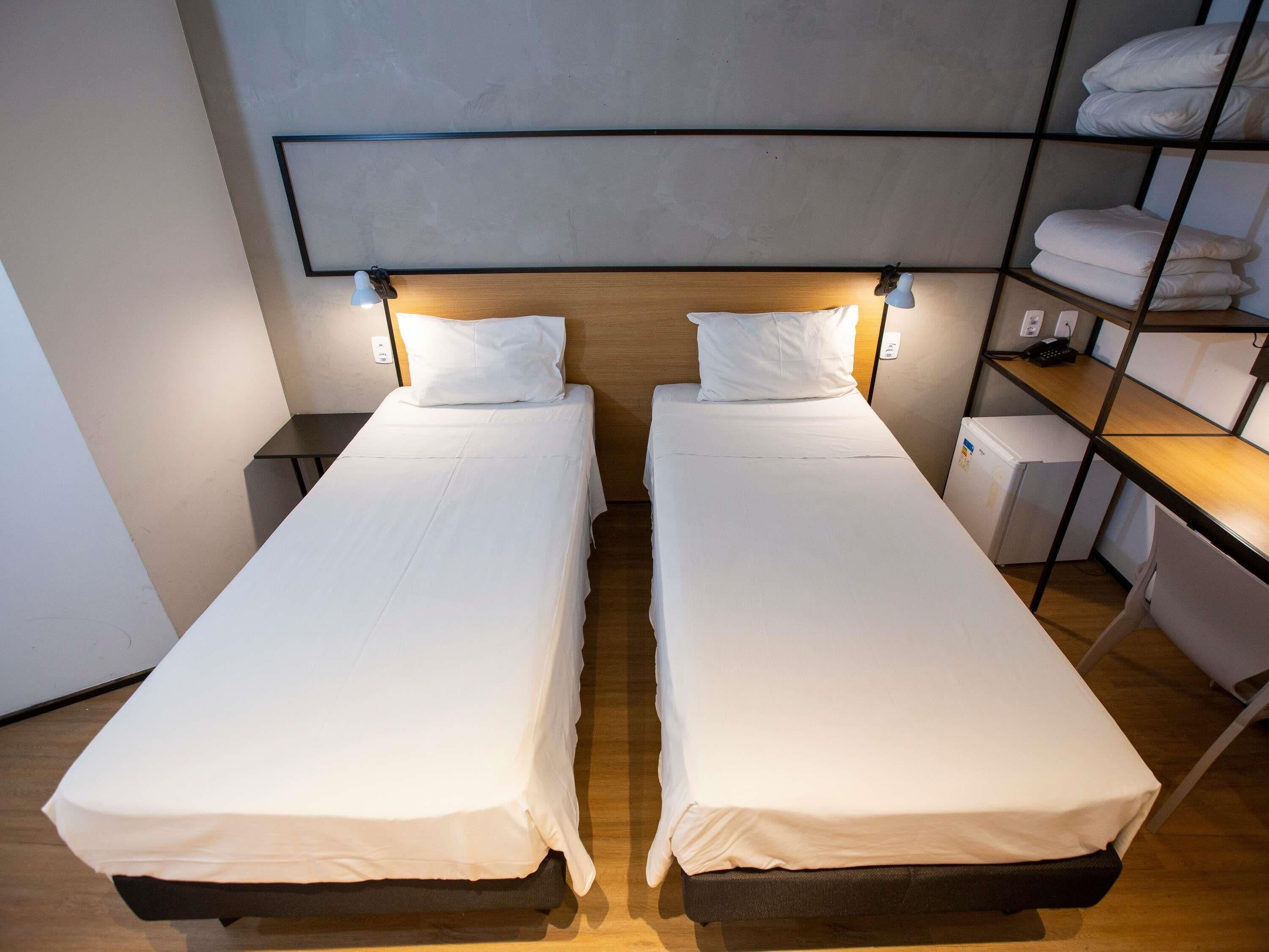 A twin room with two single beds, a wooden headboard, a small desk, and a shelf with folded towels.