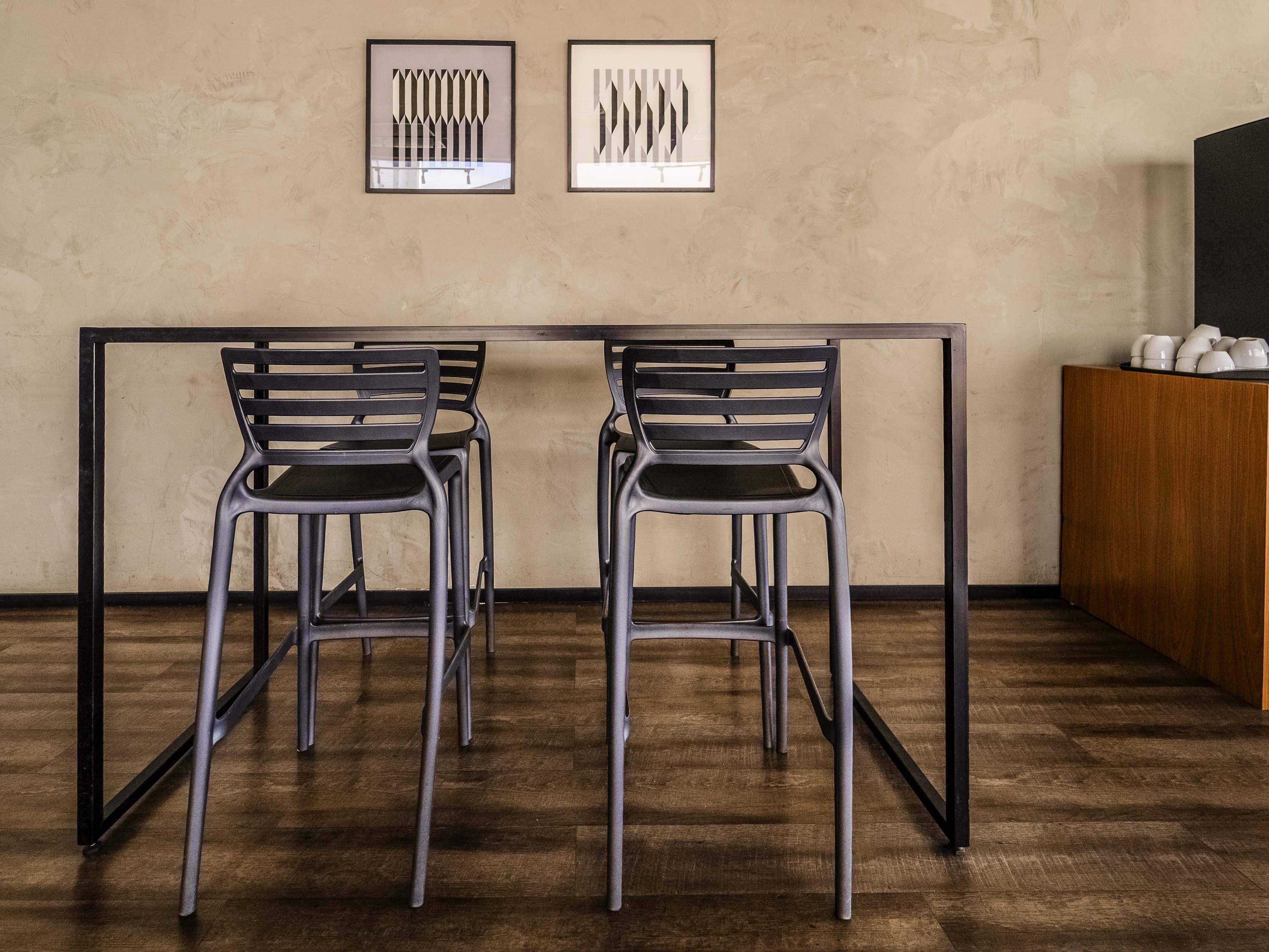 A minimalist room with a wooden floor, two metal-framed chairs, a table, and two framed abstract artworks on the wall.
