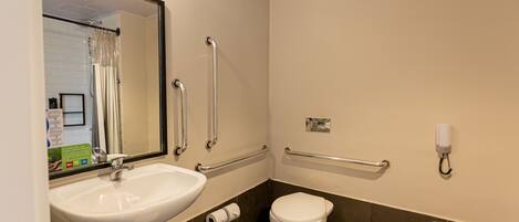 A bathroom with a white sink, a toilet, and a mirror. There are grab bars installed near the toilet and sink.