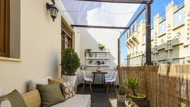 A cozy outdoor seating area with a sofa, chairs, and a small table. There is a potted plant and a bamboo fence. - Cozy duplex with Terrace, 1 Bedrooms, 2+2 Pax, Central Market, old town (Valencia)