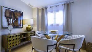 A dining area with a glass table, two white chairs, a wooden sideboard with a lamp, and a framed abstract painting on the wall. - Cozy duplex with Terrace, 1 Bedrooms, 2+2 Pax, Central Market, old town (Valencia)