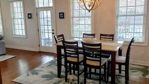 A dining area with a table, chairs, a chandelier, and large windows with blinds. - Cape Haven - Condo 1.5 Blocks from Beach (Cape Charles)