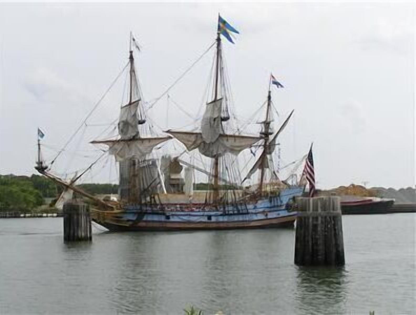 Un gran barco atracado en un muelle, con varias mástiles y banderas, incluyendo la bandera estadounidense.