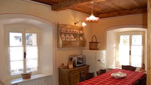 Uma área de refeições com toalha de mesa vermelha, armários de madeira, uma torradeira antiga e uma prateleira fixada na parede com objetos decorativos.