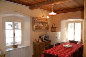 A dining area with a red tablecloth, wooden cabinets, a vintage toaster, and a wall-mounted shelf with decorative items. - EDELWEISS (PREMIA)