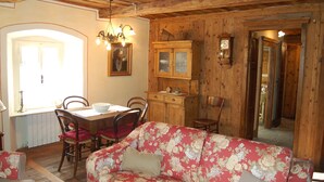 Um interior em madeira com uma mesa de jantar, cadeiras, um sofá floral e um armário com relógio.