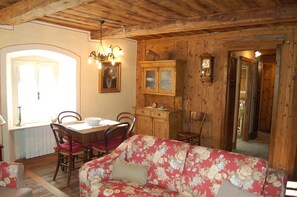 A wooden interior with a dining table, chairs, a floral sofa, and a cabinet with a clock. - EDELWEISS (PREMIA)