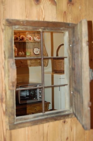 A rustic wooden interior with a small window revealing a kitchen area, including a toaster and a clock. - EDELWEISS (PREMIA)
