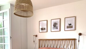 Une chambre avec un cadre de lit en bois, un luminaire suspendu en fibres tressées et trois tableaux encadrés accrochés au mur.