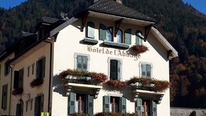 A hotel with a sign reading "Hotel de l'Abbaye" featuring a stone facade, multiple balconies with flower boxes, and a mountainous backdrop. - Breathtaking Panoramic Alpine Views (Abondance)