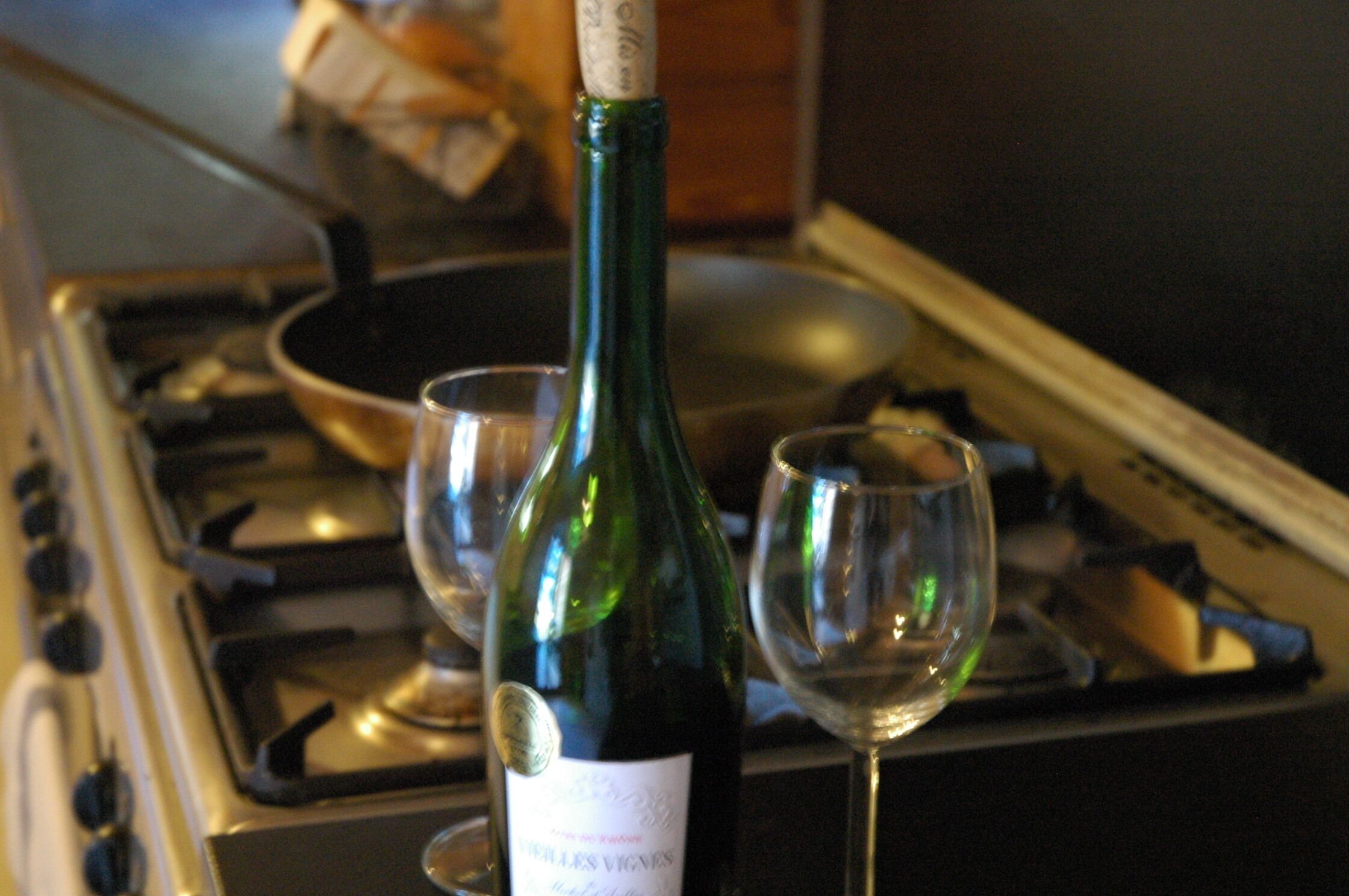 Uma garrafa de vinho e dois copos em cima do fogão.