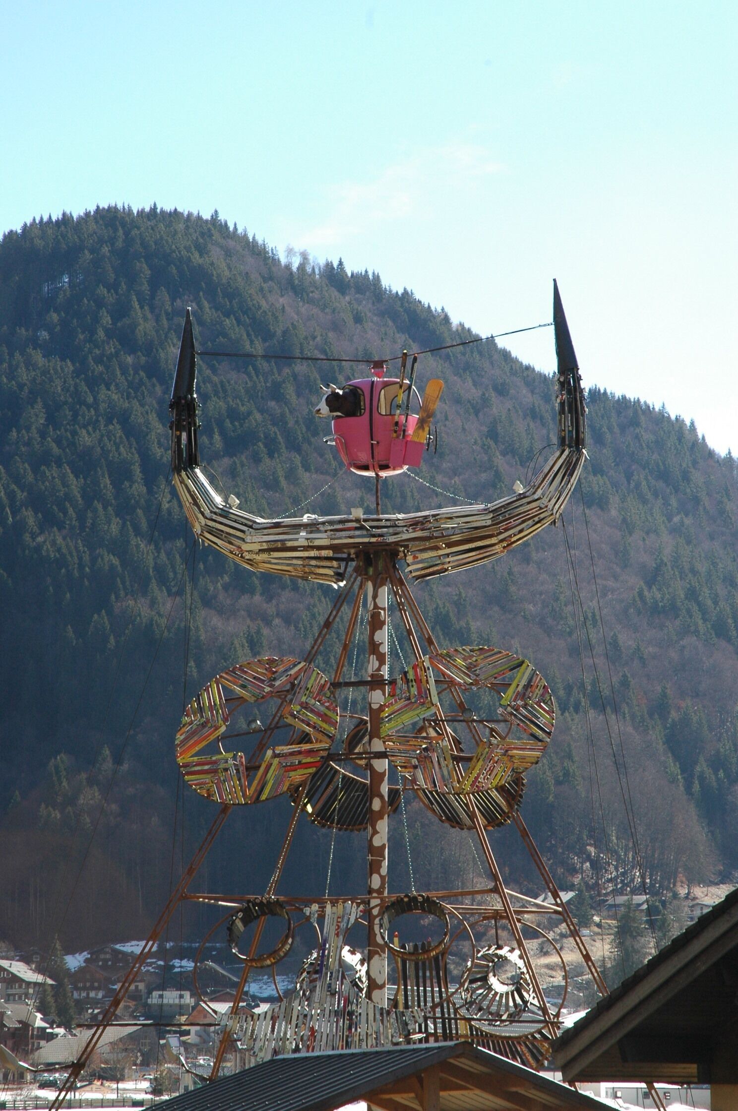 A large, ornate Ferris wheel with a gondola cabin at the top, set against a backdrop of a forested mountain.