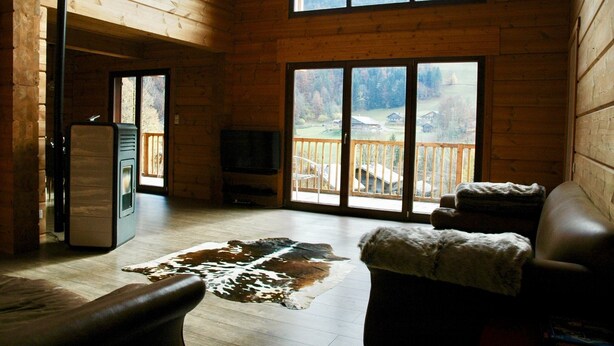 A log cabin interior with a large window, a fireplace, and a leather sofa. - Breathtaking Panoramic Alpine Views (Abondance)