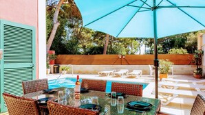 Un espace extérieur avec une piscine, une table et des chaises, une bouteille de vin et un grand parasol.
