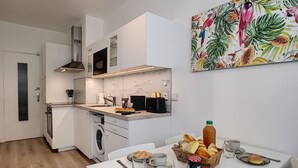 A modern kitchen with a built-in oven, microwave, and washing machine. There is a dining area with a table set for breakfast, including bread, pastries, and a bottle of juice. - N&J  - BEETHOVEN - Central - Residental area (Niza)