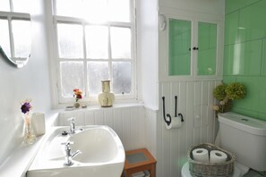Un bagno con un lavandino bianco, una finestra, un WC e piastrelle verdi.