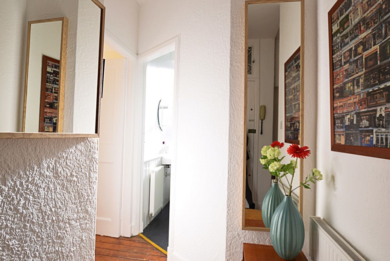 A hallway with a textured wall, a mirror, and a door leading to another room. There are two vases with flowers on the wall.