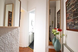 A hallway with a textured wall, a mirror, and a door leading to another room. There are two vases with flowers on the wall.