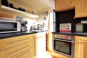 Una cucina moderna con mobili in legno, un forno a microonde, una macchina per il caffè e un bollitore. Sul muro è presente un cartello e sul bancone c'è un libro intitolato