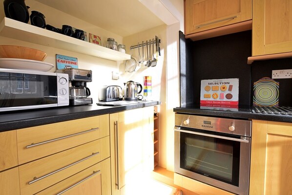 A modern kitchen with wooden cabinets, a microwave, a coffee maker, and a kettle. There is a sign on the wall and a book titled "Classic Selection" on the counter.