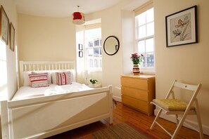 A bedroom with a white bed, a dresser, a chair, and a window with natural light.