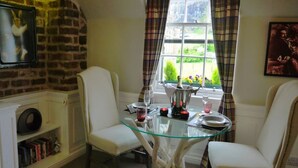 A dining area with a glass table, white chairs, a fireplace, and a window with curtains. - Charming Nest for Two with Castle View (Edinburgh)